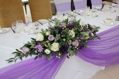 the table is set with purple and white flowers, greenery, and napkins