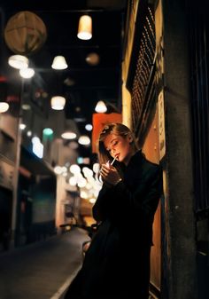 a woman leaning against a wall while looking at her cell phone in the dark,