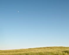 a grassy field under a blue sky with an object in the distance on top of it