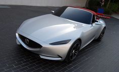 a silver sports car parked in front of a building on a brick road with two red cars behind it