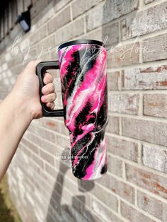 a hand holding a pink and black coffee mug in front of a brick wall with graffiti