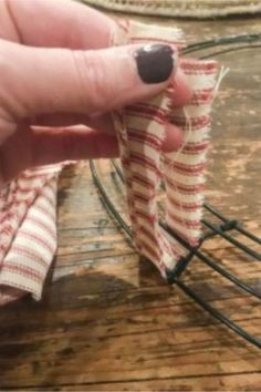 a hand holding a piece of fabric on top of a wooden table next to wire