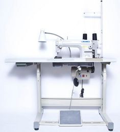 a sewing machine sitting on top of a white table next to a monitor and keyboard