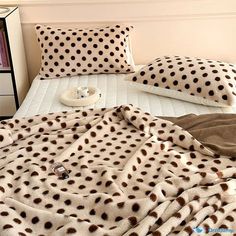 a bed covered in brown and white polka dot pillows next to a night stand with books on it