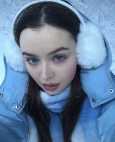 a woman with long hair wearing a blue jacket and white fur hat, in the snow