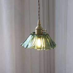 a green lamp hanging from a ceiling in front of a white curtained wall with curtains behind it