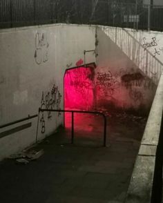 a dark tunnel with graffiti on the walls and red light at the entrance to it