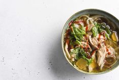 a bowl of chicken noodle soup on a white surface