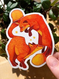 a hand holding up a sticker with two foxes on it