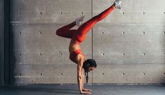 a woman doing a handstand on one leg in front of a concrete wall