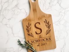 a wooden cutting board with the letter s on it and an olive sprig