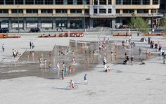 many people are playing in the water near a large building and some buildings with windows