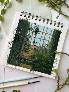 an open notebook sitting on top of a table next to some plants and pencils