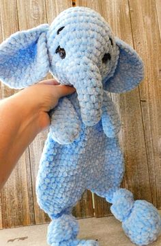 a hand holding an elephant stuffed animal in front of a wooden wall with planks