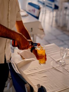 a man pouring beer into a glass on top of a white tablecloth covered table