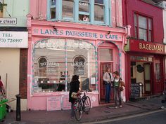 people are standing on the sidewalk in front of a store with pink walls and windows