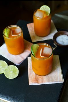 three glasses filled with drinks sitting on top of napkins next to lime wedges