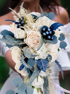 a bridal bouquet with white roses and blue berries on the bride's bouquet