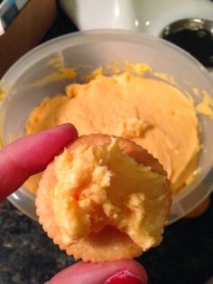 a person holding up a doughnut in front of a bowl with orange frosting