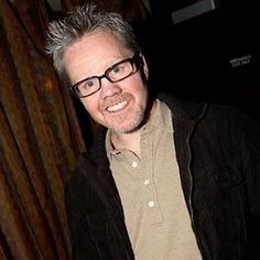 a man wearing glasses standing in front of a curtain