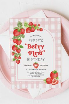 a pink and white plate with strawberries on it next to a card that says berry first birthday