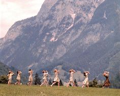 a group of women walking across a lush green field next to a tall mountain covered in snow