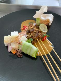 a black plate topped with meat and veggies next to chopsticks on a table