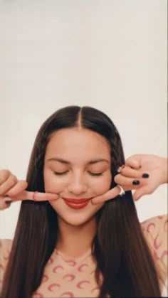 a woman with long hair holding her hands up to her face and looking at the camera