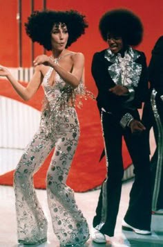 two women in disco outfits are dancing on the dance floor with one woman holding her hand out