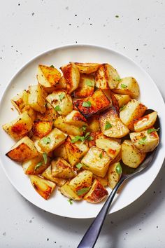 a white plate topped with cooked potatoes on top of a table next to a fork