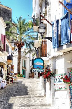 an alley way with clothes hanging from the balconies and palm trees on either side