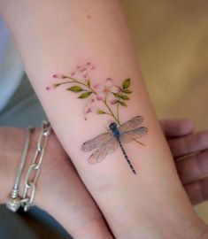 a woman's arm with a dragonfly and flower tattoo on the left wrist