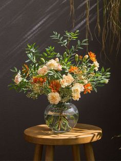 a vase filled with orange and white flowers on top of a wooden table next to a black wall