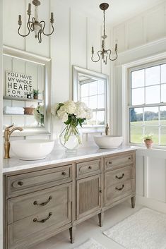 a bathroom with two sinks and mirrors on the wall next to each other in front of windows