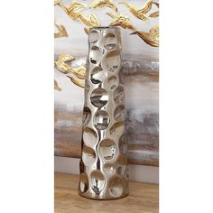 a silver vase sitting on top of a wooden table next to a wall with gold leaves