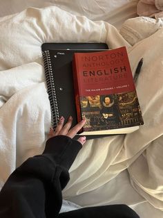 a person holding a book on top of a white bed covered in sheets and blankets