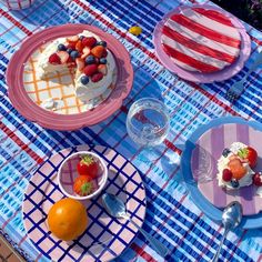 a table topped with plates covered in cake and fruit next to water glasses on top of a checkered cloth