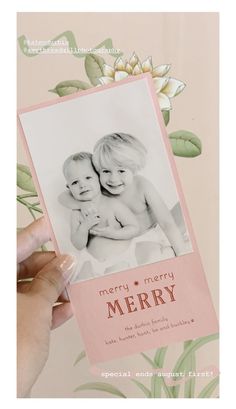 a person holding up a card with a picture of two babies on it and flowers in the background