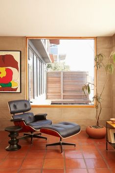 an eames chair and ottoman in the corner of a room with a large window