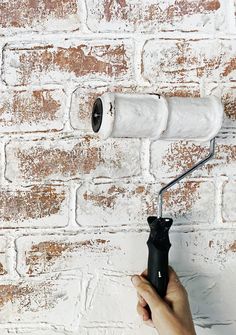 a person holding a paint roller in front of a brick wall with white paint on it