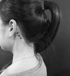 the back of a woman's neck with small birds on her left side ear