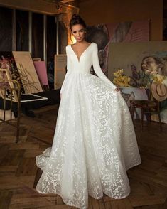 a woman in a white wedding dress standing on a wooden floor with paintings behind her