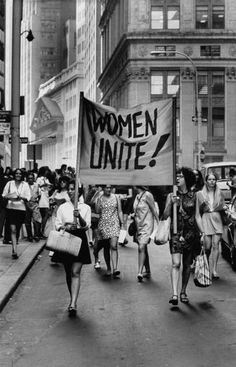 black and white photograph of women marching down the street holding signs that read women united