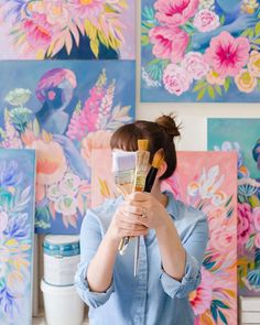 a woman holding a paintbrush in front of paintings