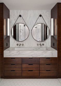 a bathroom with marble counter tops and two mirrors on the wall above it, along with wooden cabinets