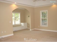 an empty living room with beige walls and white shutters on the window sill