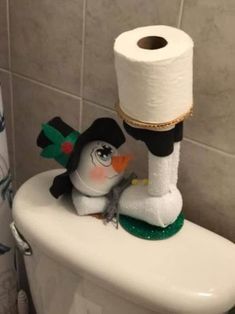 a toilet with two rolls of toilet paper on top of it and a toy penguin in the middle