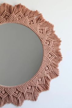 a round mirror with tassels hanging on the wall next to a white wall