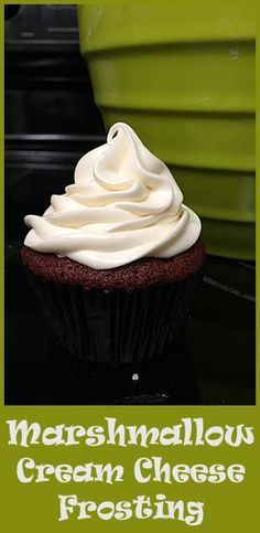 a cupcake with white frosting sitting on top of a black table next to a green bucket