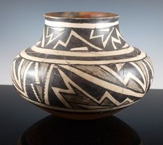 a black and white vase sitting on top of a table next to a gray wall